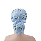 A light blue hydrangea floral surgical scrub cap with green leaves and a matching light blue ribbon bow, shown from the back on a head.