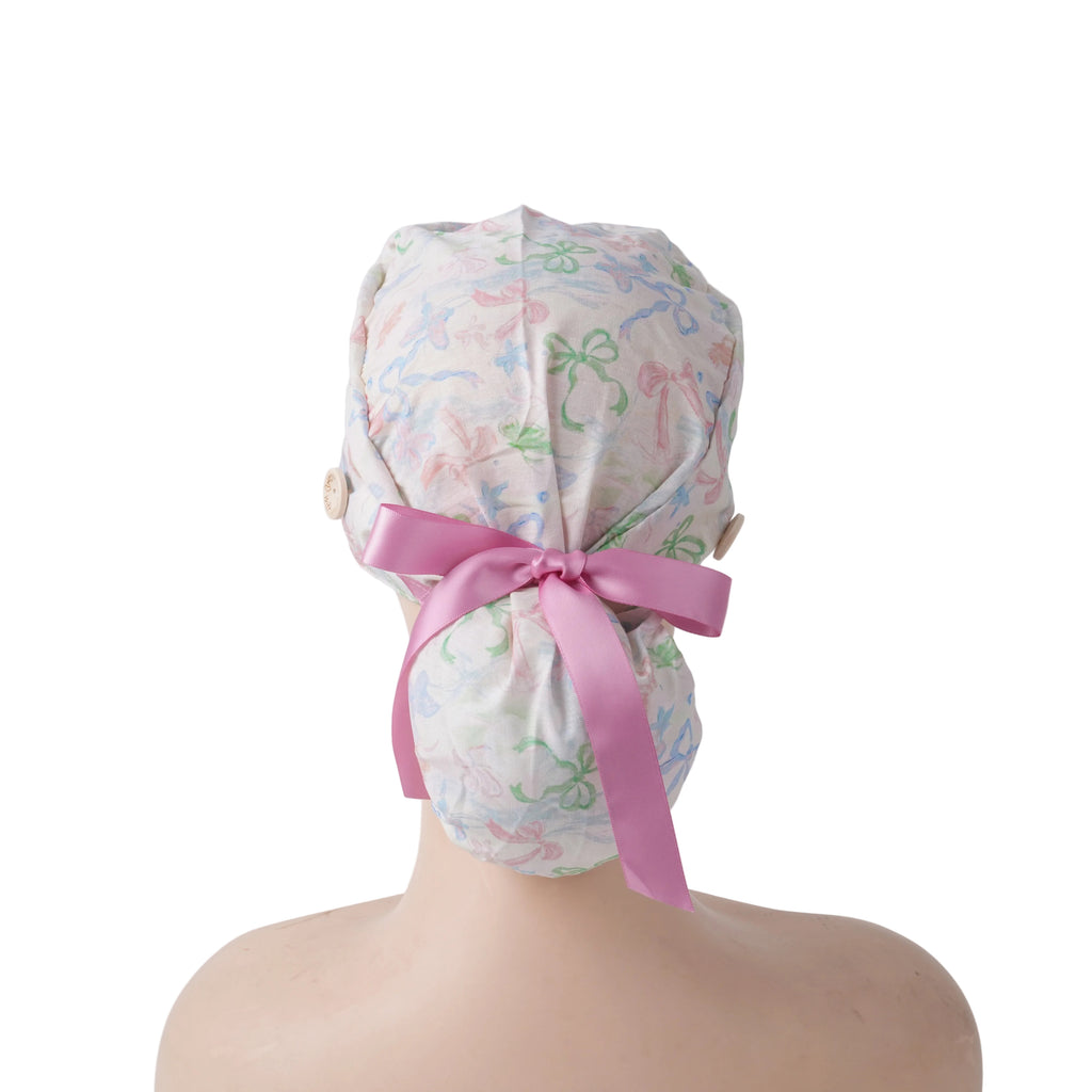 A ponytail cap with pastel multicolor bows print and a prominent pink satin ribbon tied at the back.