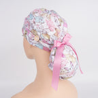 A ponytail hat featuring a butterfly pattern in soft pink tones, adorned with pink ribbon, displayed on a mannequin head,  viewed from a left-side angle.