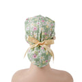 back view on mannequin of sage green daisy floral scrub cap with yellow satin ribbon bow.