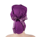 A dark purple ponytail scrub cap with a matching satin ribbon bow, shown from the back on a mannequin head.
