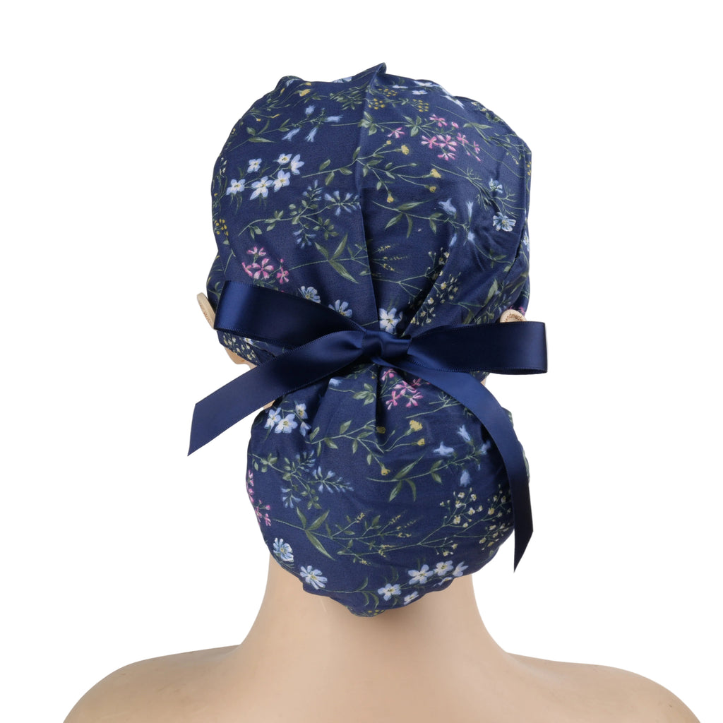 A navy blue ponytail scrub cap with delicate multicolor floral print and a matching navy ribbon bow.