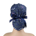 A navy blue ponytail scrub cap with delicate multicolor floral print and a matching navy ribbon bow.
