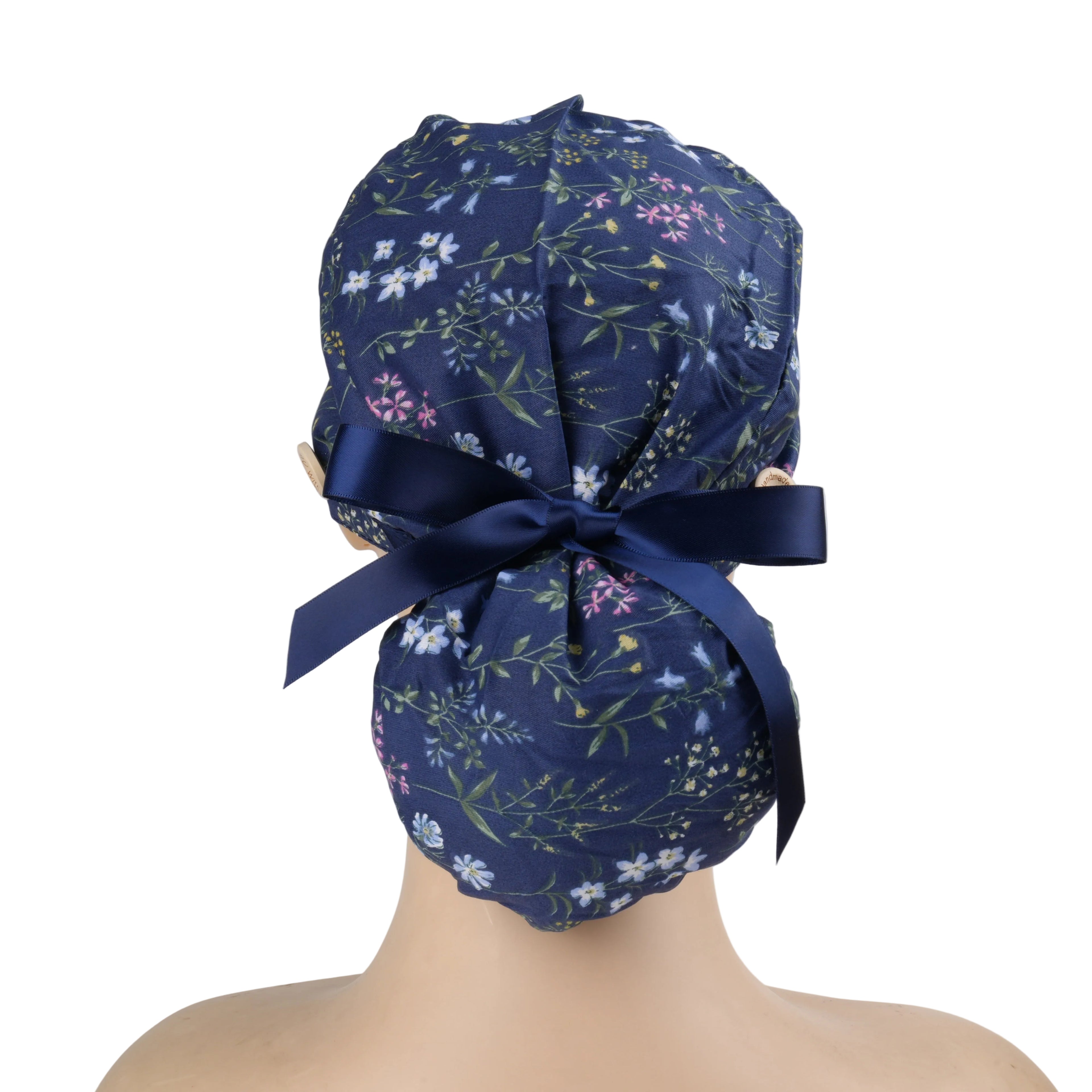 A navy blue ponytail scrub cap with delicate multicolor floral print and a matching navy ribbon bow.