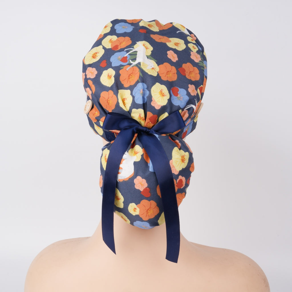 A floral patterned ponytail scrub cap with a navy blue satin bow, displayed on a mannequin head.