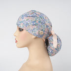 A blue, pink floral-patterned ponytail surgical cap displayed on a mannequin head in profile against a light gray background. 