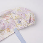Lavender iris floral ponytail scrub cap close-up, ribbon stitching and wooden button detail.