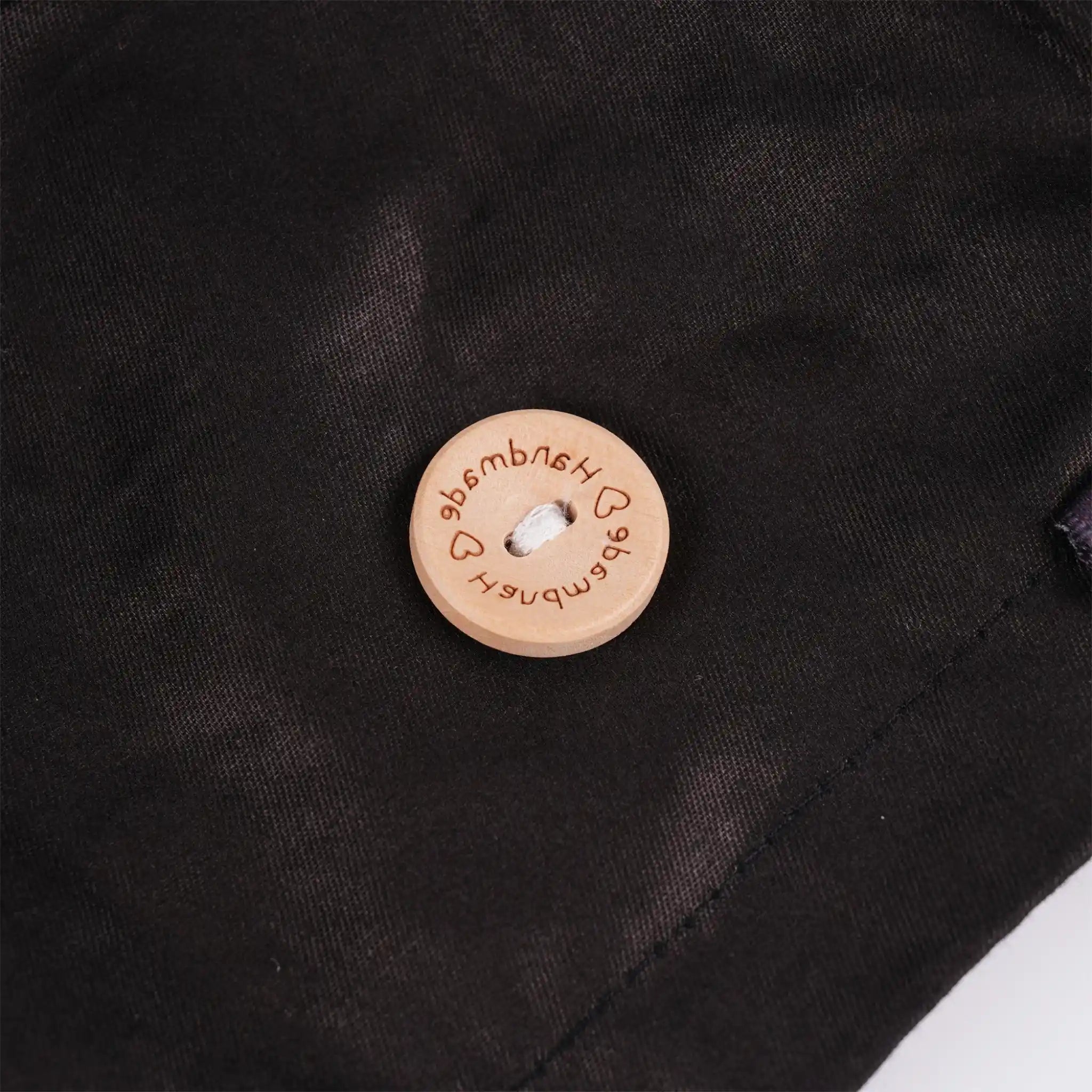 A close-up of a wood mask button engraved with the brand name 'handmade' and heart icons.