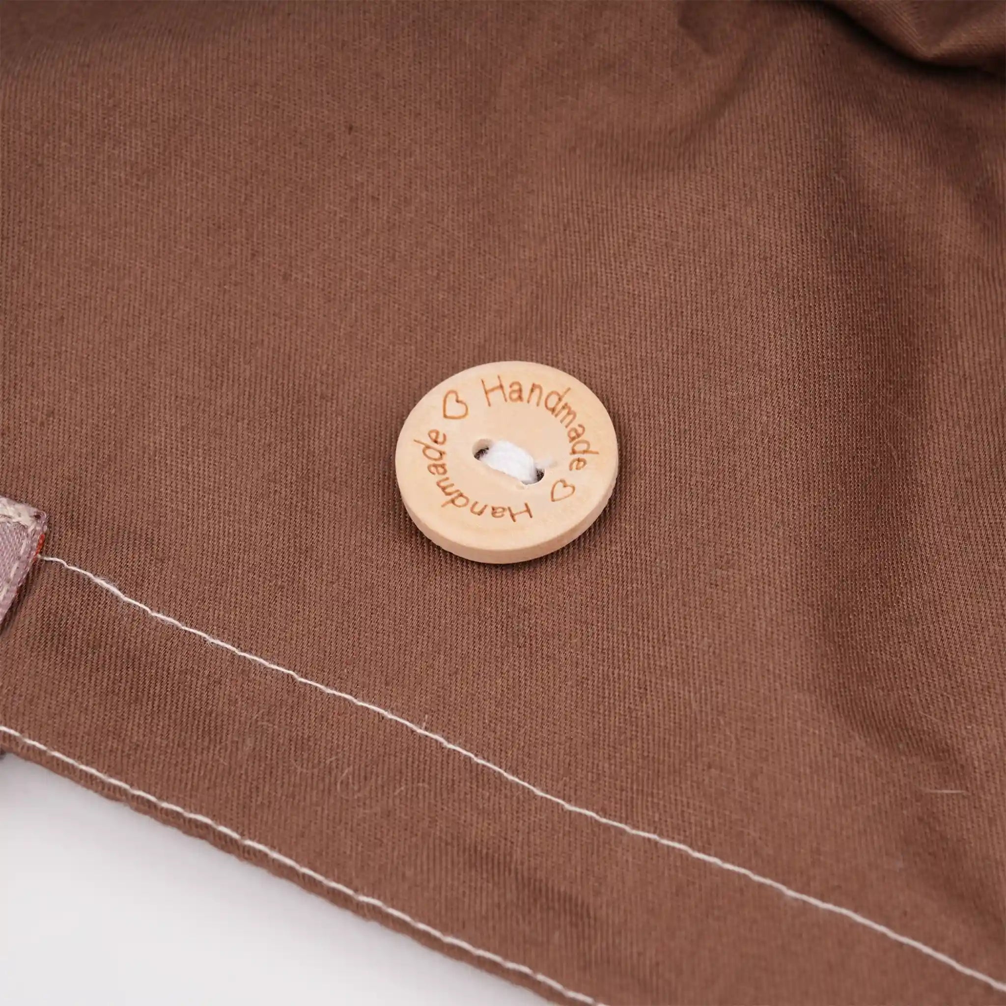 Close-up of the button on a brown ponytail hat, engraved with 'Handmade' and heart.
