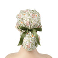 A ponytail cap with squirrels and botanical print in sage green, tied with a dark green satin ribbon at the back.