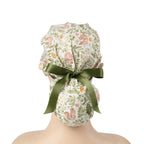A ponytail cap with squirrels and botanical print in sage green, tied with a dark green satin ribbon at the back.