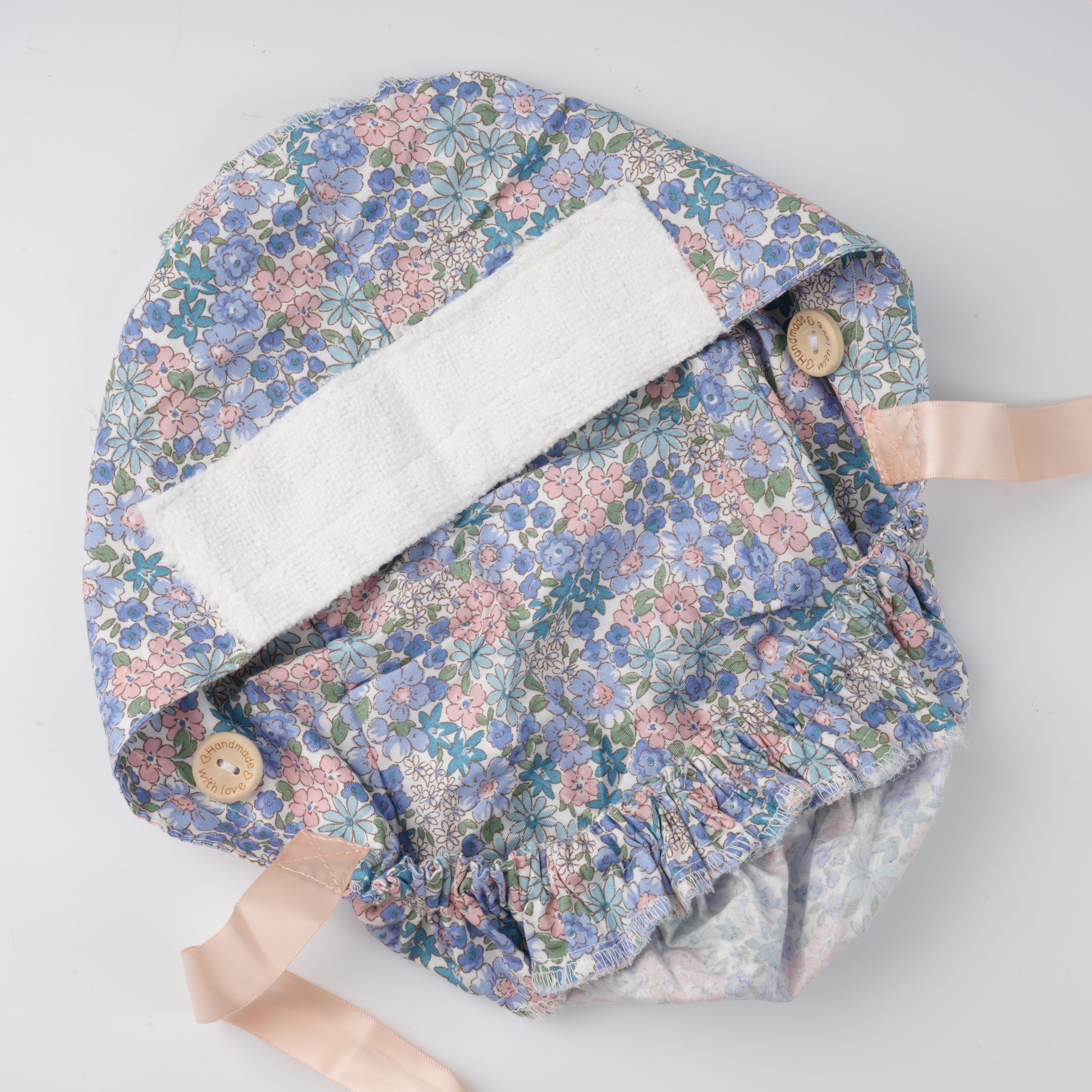 Interior view of the ponytail hat, white sweatband on the forehead, wooden mask buttons and satin ribbons on both sides,  laid flat on a light gray background.